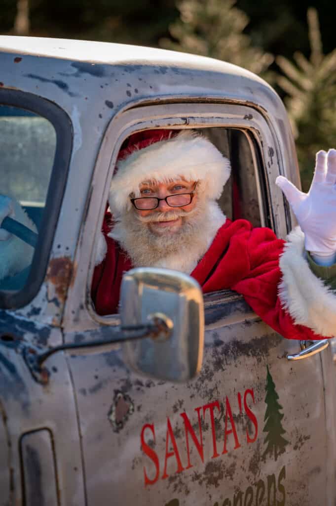 Santa in old pickup truck waving out the driver's side open window.